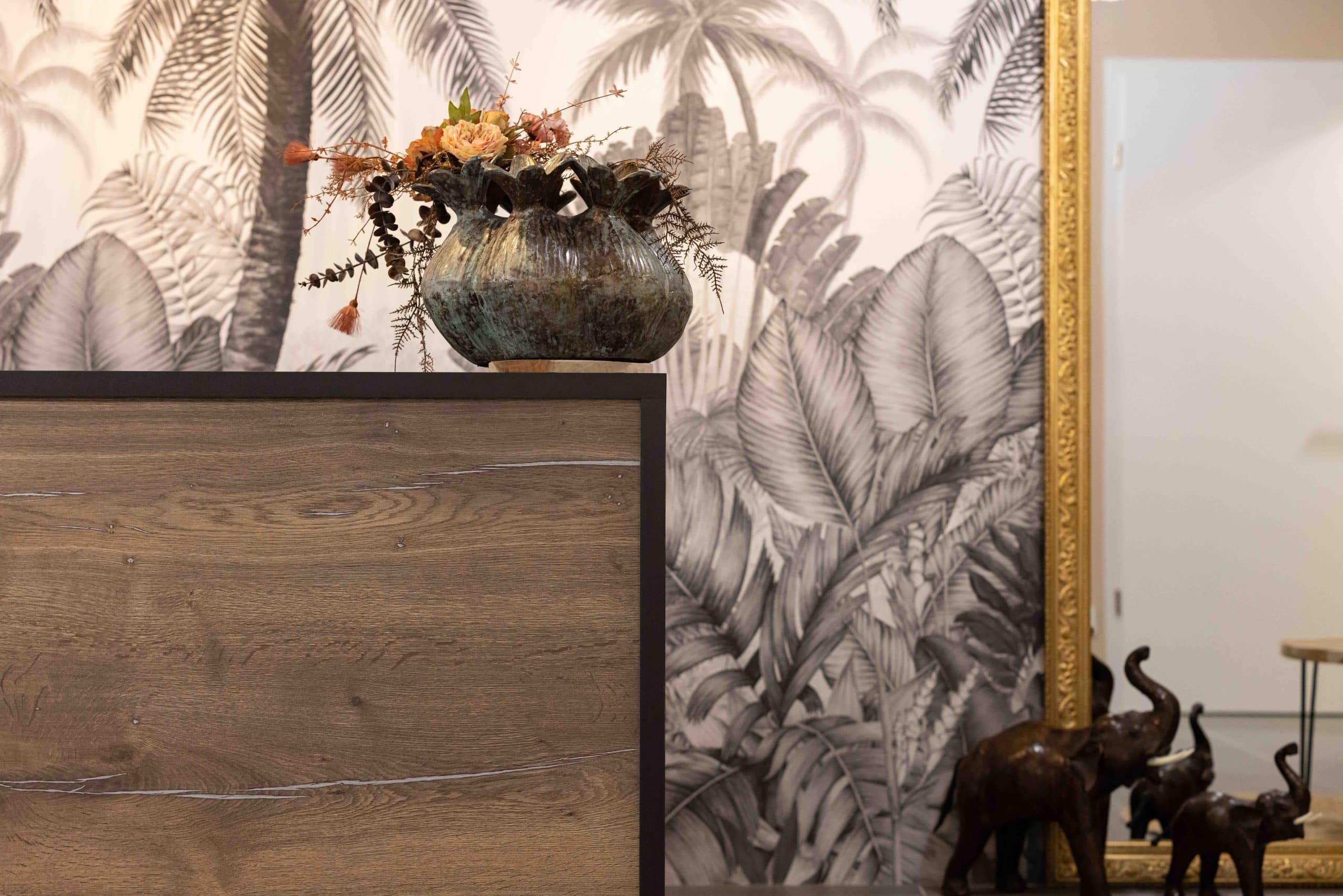 Détail déco de la boutique Osmose by Charly avec grand miroir doré, vase en céramique et statues d’éléphants, sur fond de fresque tropicale, mis en scène par Alena Zuliani – Azai, architecte d’intérieur en Alsace.